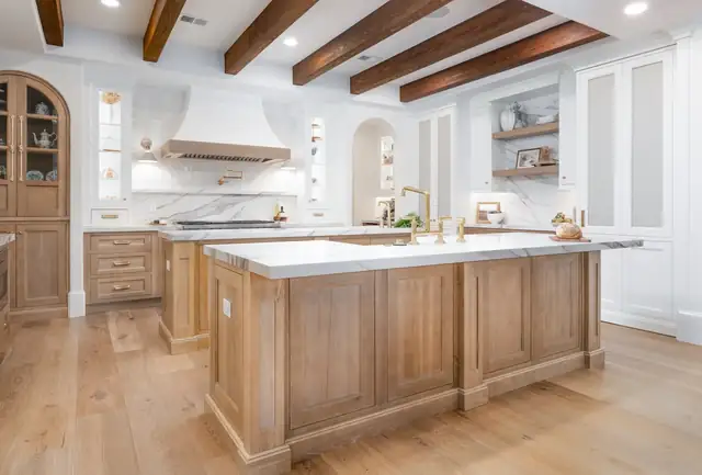 Kitchen by KBF Design Gallery with a white oak island, marble waterfall top, brass fixtures, a plaster hood and exposed wood ceiling beams