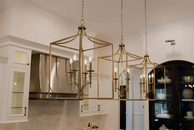 Three brass cage lanterns over a kitchen island with a curved stainless hood, white cabinetry and a dark arched hutch