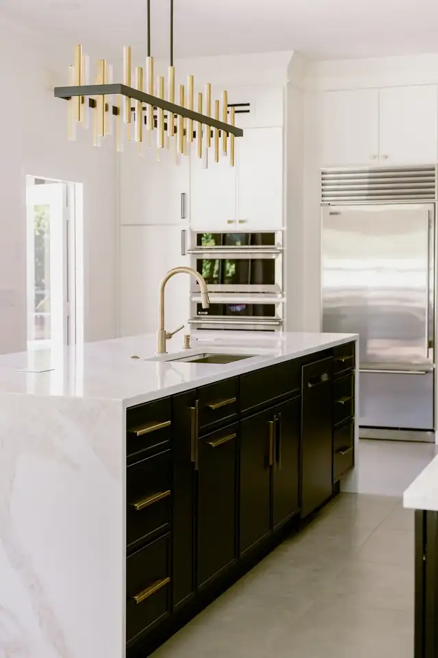 Dommerich Estates kitchen in Maitland with a black center island, white waterfall counter, brass linear chandelier and stainless refrigerator