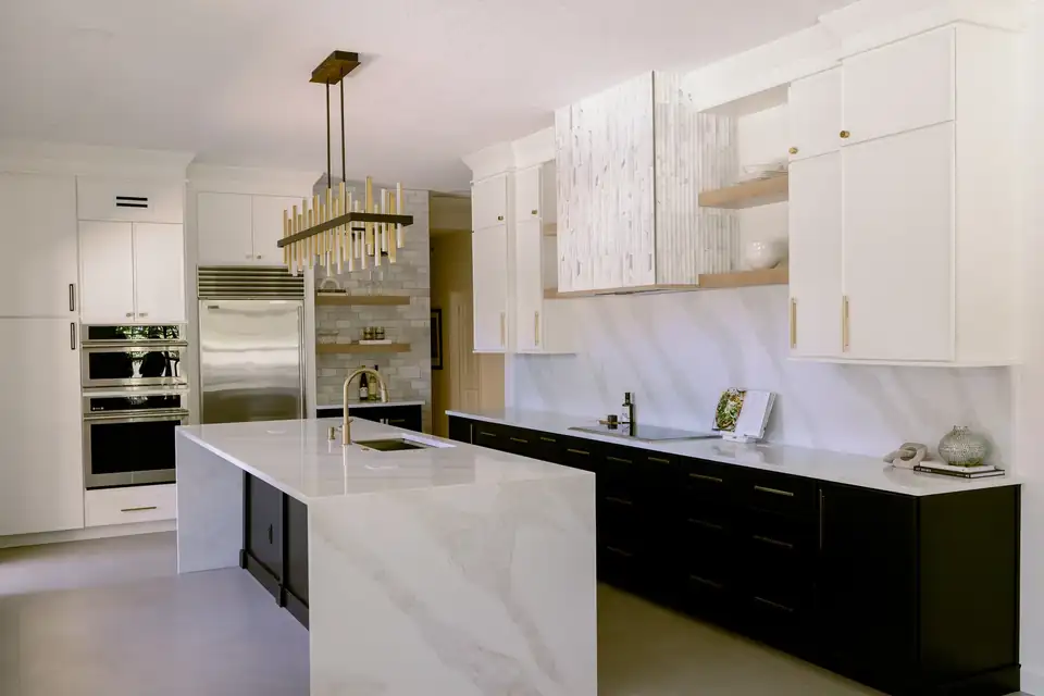 Kitchen remodeling Maitland: Dommerich Estates kitchen with a marble waterfall island, brass-and-black linear chandelier, black lower cabinets with brass pulls and wall ovens