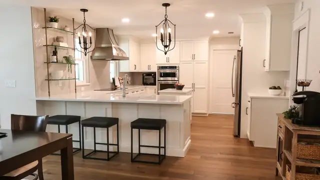 Maitland whole-home renovation kitchen with a white quartz peninsula, black counter stools, stainless chimney hood and brass-and-glass shelves on herringbone tile