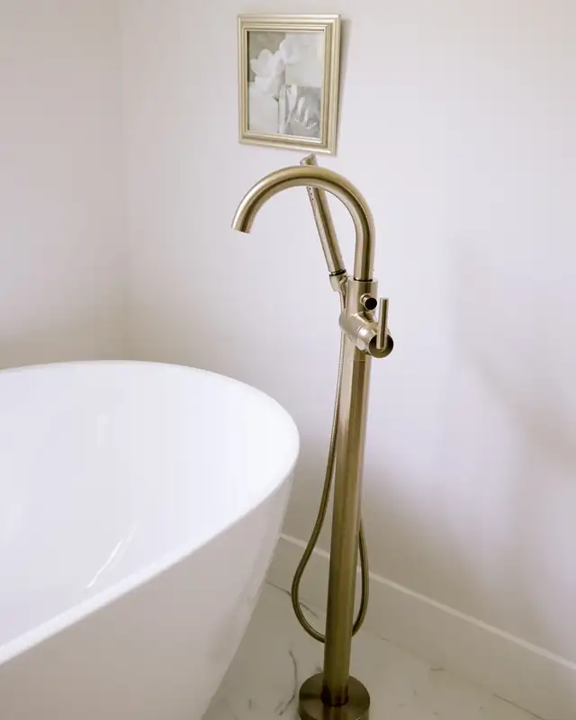 Maitland primary bath detail with a white freestanding soaking tub and brass floor-mounted tub filler on marble-look tile