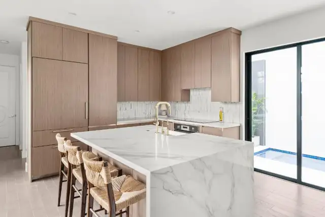 Winter Park townhome kitchen with rift-cut oak slab cabinets, a marble waterfall island, woven counter stools and glass doors to a pool courtyard