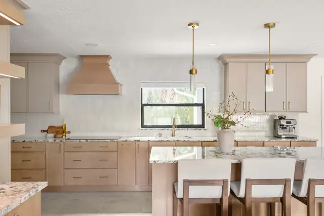 Winter Park whole-home renovation kitchen with white-oak cabinetry, a custom tapered hood, brass pendants and an island with upholstered stools